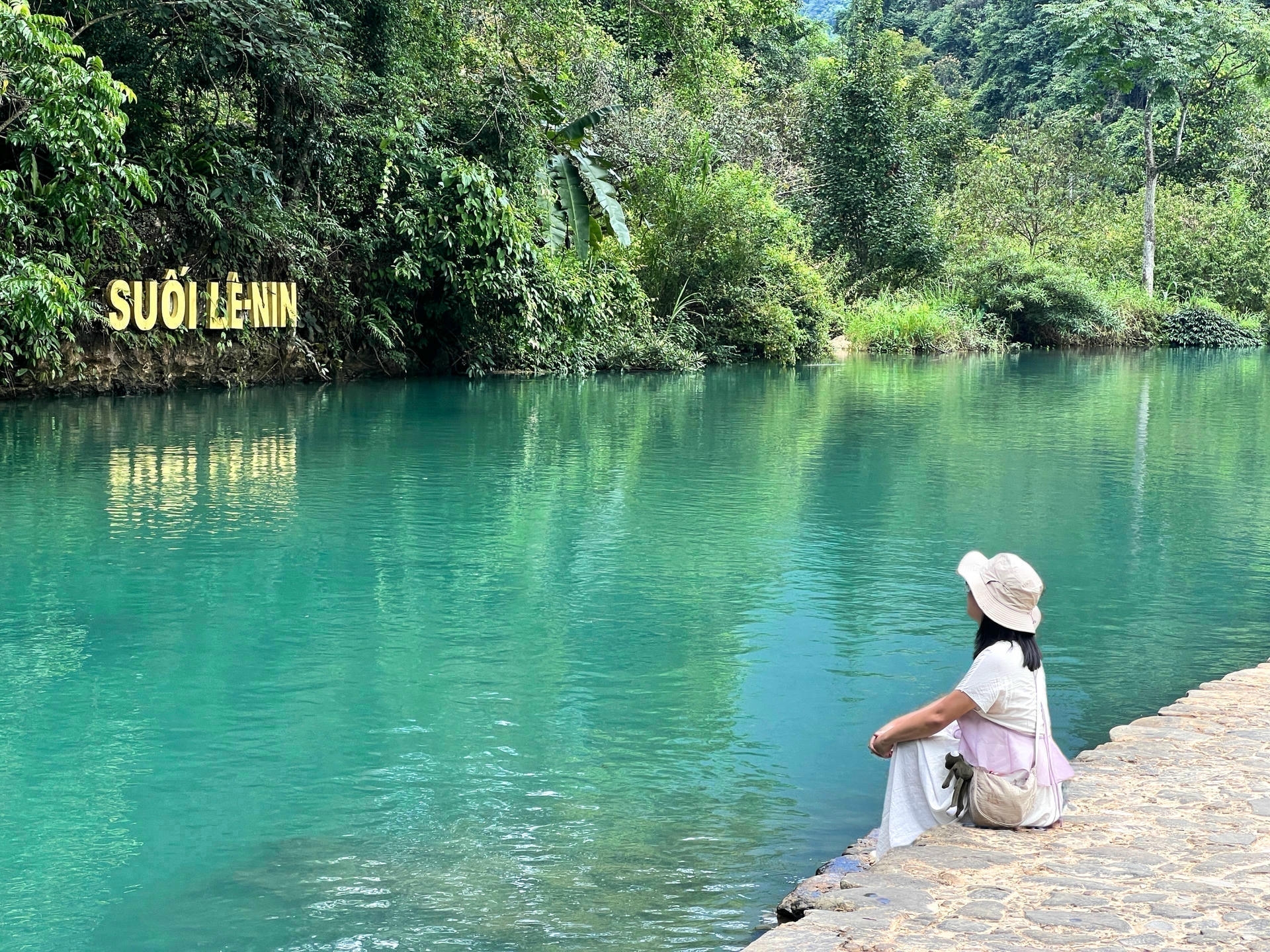 Traveler sitting by the clear turquoise water of Lenin Stream on the Cao Bang Loop in Vietnam